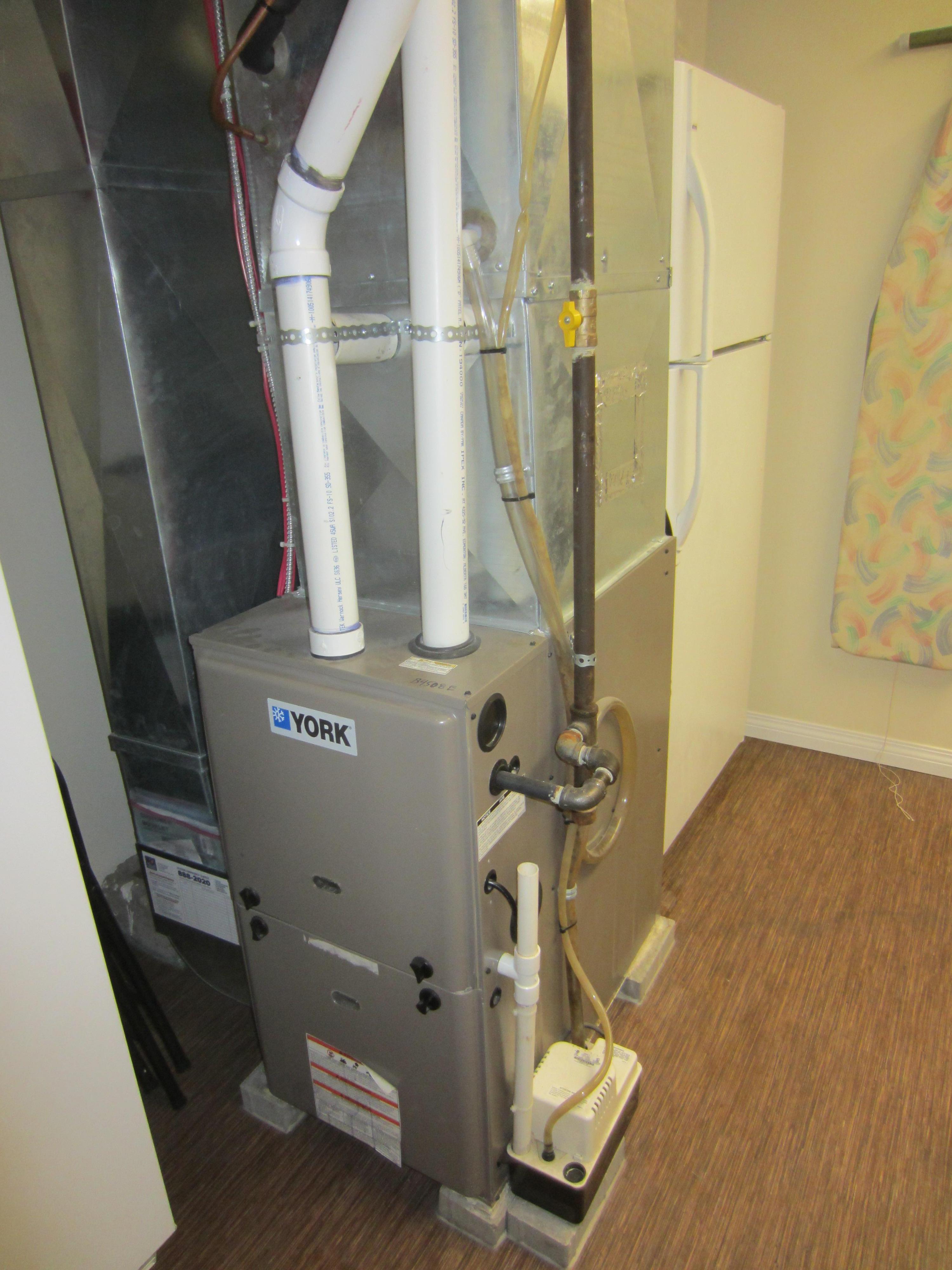 Residential gas furnace with ductwork and PVC vent pipes.